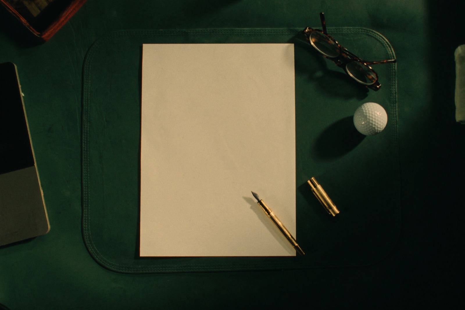 A blank ivory card and brass pen on a green leather desk
